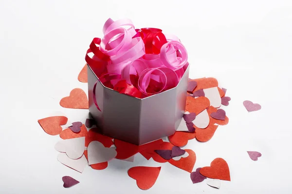 Décorations festives. Rubans rouges et roses dans une boîte sur fond blanc. Non loin de là se trouvaient des coeurs en papier coloré. Concept de célébration . — Photo