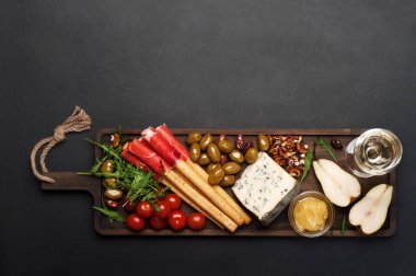 Akdeniz ürünlerde (jambon, mavi peynir, roka, kiraz, fındık) kahverengi kesme tahtası. Koyu arka plan. Yararlı doğal taze yiyecek. Metin için yer