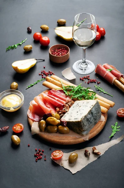 Mediterranean products (ham, blue cheese, arugula, cherry, nuts) on a brown cutting board. Dark background. Useful natural fresh food — Stock Photo, Image