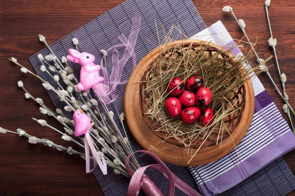 Uova di quaglia rosa sul fieno nel cesto su un tovagliolo viola. Fondo in legno scuro. Concetto Arredo pasquale e cibo — Foto Stock