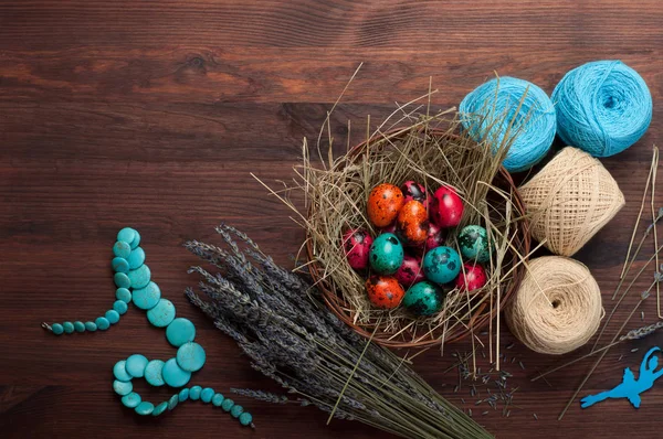 Sfondo pasquale. Uova multicolori in un cesto, fiori, grovigli di filo e decorazione su uno sfondo di legno marrone. Spazio per il testo (spazio libero ) — Foto Stock