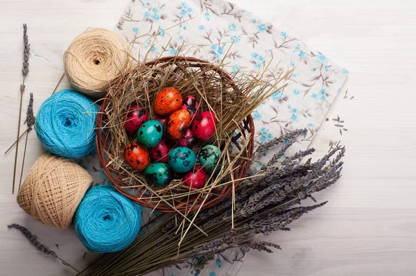 Sfondo pasquale. Uova multicolori in un cesto, fiori, grovigli di filo e decorazione su uno sfondo di legno bianco . — Foto Stock
