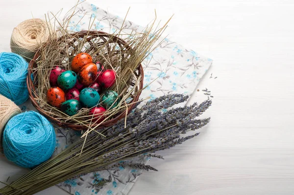 Easter background. Multicolored eggs in a basket, flowers, tangles of thread and decoration on a white wooden background. Space for text (free space) — Stock Photo, Image