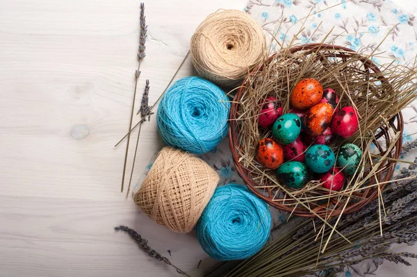 Easter background. Multicolored eggs in a basket, flowers, tangles of thread and decoration on a white wooden background. Space for text (free space) — Stock Photo, Image