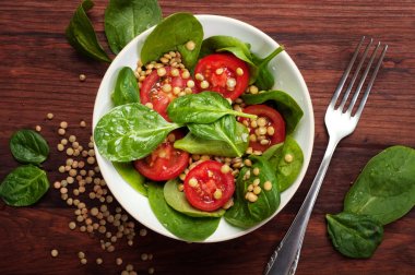 Salata bebek ıspanak yaprakları, yeşil mercimek, domates, zeytin yağı ve bir kahverengi ahşap yüzeyde bir kapta limon suyu. Bir diyet yemek. Vejetaryen, vegan kavramı 