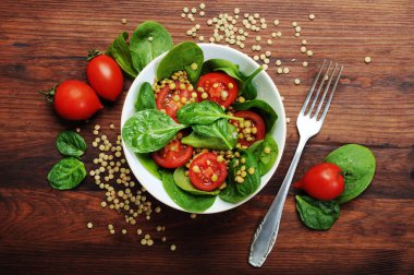 Salata bebek ıspanak yaprakları, yeşil mercimek, domates, zeytin yağı ve bir kahverengi ahşap yüzeyde bir kapta limon suyu. Bir diyet yemek. Vejetaryen, vegan kavramı 