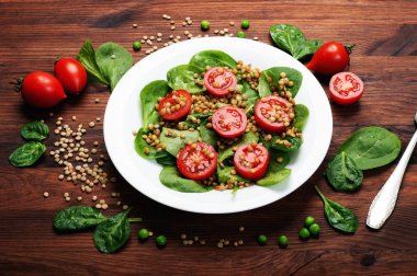 Salata bebek ıspanak yaprakları, yeşil mercimek, domates, zeytin yağı ve bir kahverengi ahşap yüzeyde bir kapta limon suyu. Bir diyet yemek. Vejetaryen, vegan kavramı 