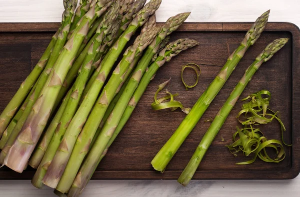 Asparagi crudi su un tagliere di legno sullo sfondo bianco. Cornice ritagliata. Vegetariano, concetto vegano — Foto Stock