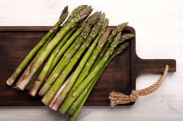 Espárragos crudos en una tabla de cortar de madera sobre un fondo blanco. Marco recortado. Vegetariano, concepto vegano —  Fotos de Stock