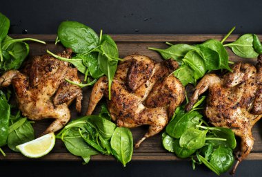 Kahverengi kesme tahtasının üzerinde, ıspanağın yanında kızarmış bıldırcın.