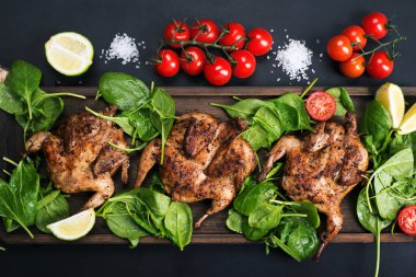 Kahverengi kesme tahtasının üzerinde ıspanağın yanında ızgara bıldırcın., 