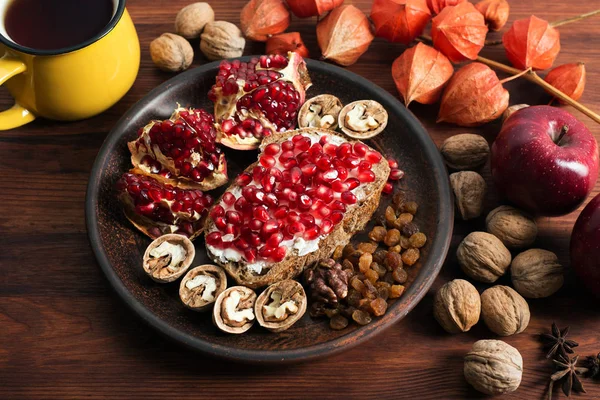 Micul dejun rapid și sănătos. Sandwich cu brânză moale și semințe de rodie, nuci, stafide și ceai pe o placă de lemn maro — Fotografie, imagine de stoc