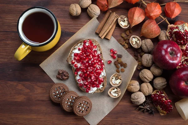 Desayuno rápido y saludable. Sandwich con queso suave y semillas de granada, nueces, pasas y té en una tabla de madera marrón — Foto de Stock