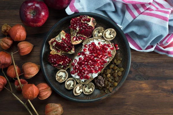 Quick and healthy breakfast. Sandwich with soft cheese and pomegranate seeds, nuts and raisins on a brown wooden board — Stock Photo, Image