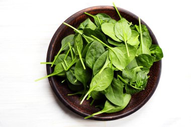 Beyaz arka planda kahverengi bir tabakta taze, sulu taze ıspanak.