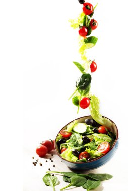 Yiyecek havalanması: Beyaz arka planda kaseye düşen bir salata. Mesaj için yer. Seçici keskinlik