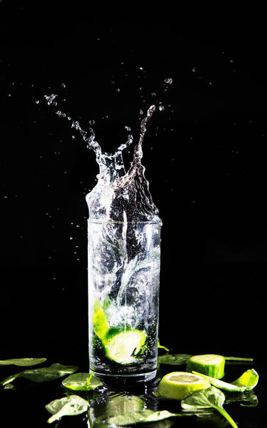 Cucumber water that spills out of a glass on a black background.