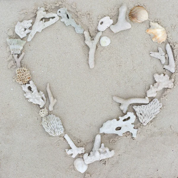 Seashells and corals heart frame on sand background.