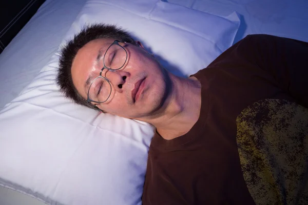 Asya adam üstünde onun gözüne gözlük ile yatakta uyumak — Stok fotoğraf