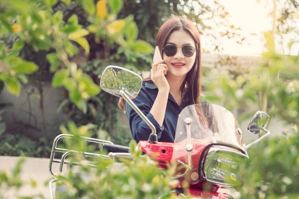 年轻快乐的亚洲女人谈她的电话，在她的摩托车 — 图库照片