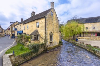 Bourton On Water adlı bir nehir boyunca eski taş binalar standı,