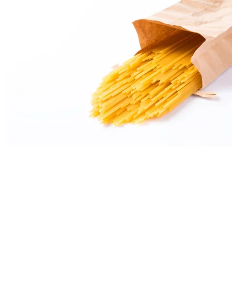 Raw spaghetti noodle spilling out of brown paper bag, white back — Stock Photo, Image