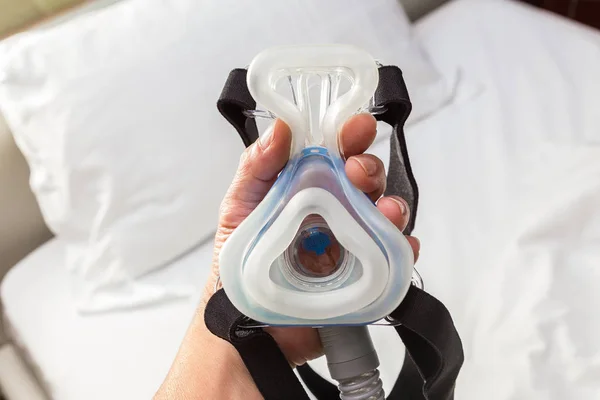 Чоловіча рука тримає маску CPAP, з'єднуючись з ремінцем і шлангом, на борту — стокове фото