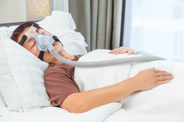Orta yaş Asya adam CPAP maske gerekçesini takmış yatağında uyuyan