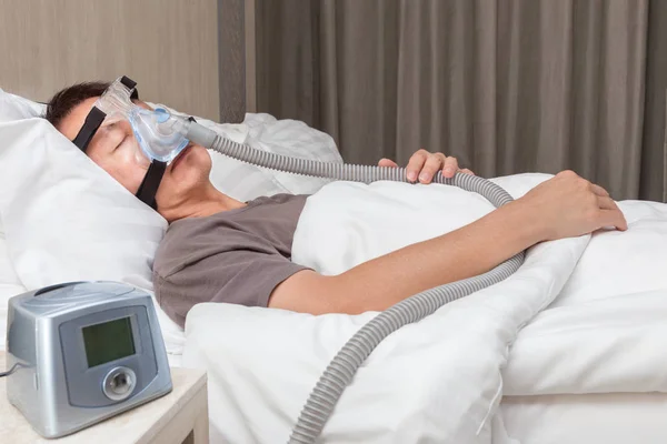 Orta yaş Asya adam CPAP maske gerekçesini takmış yatağında uyuyan