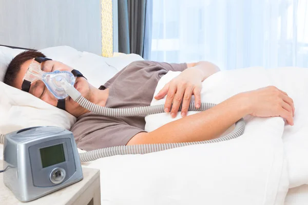 Середнього віку азіатський чоловік спить в масці CPAP, що з'єднується з ефіром — стокове фото