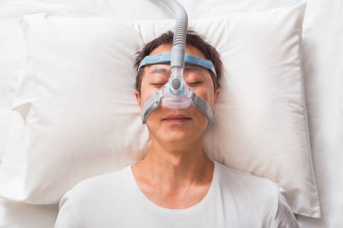 Orta yaş Asya adam CPAP maske gerekçesini takmış yatağında uyuyan