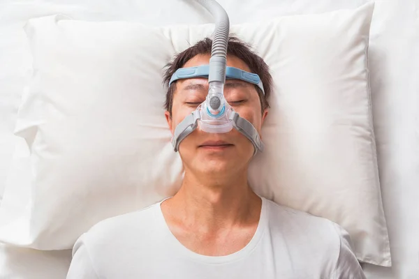 Orta yaş Asya adam CPAP maske gerekçesini takmış yatağında uyuyan