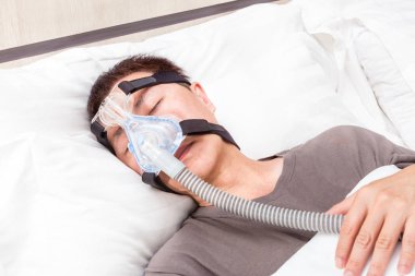 Orta yaş Asya adam CPAP şapkalar m takmış yatağında uyuyan