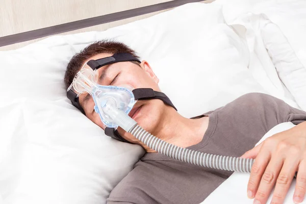 Mezza età asiatico uomo dormire in suo letto indossare CPAP copricapo m — Foto Stock