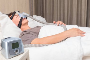 Orta yaş Asya adam CPAP maske gerekçesini takmış yatağında uyuyan
