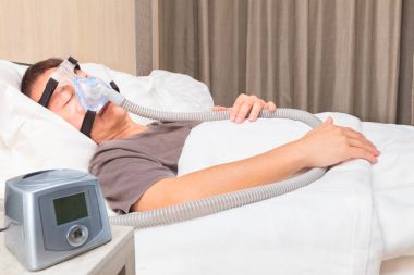 Orta yaş Asya adam CPAP maske BAGLANTINIZI giyen yatakta uyuyor