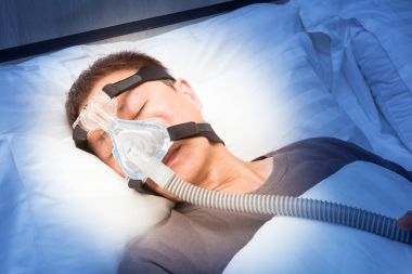 Orta yaş Asya adam CPAP maske gerekçesini takmış yatağında uyuyan