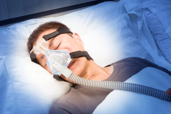 Orta yaş Asya adam CPAP maske gerekçesini takmış yatağında uyuyan