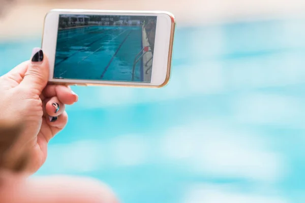 Hand van de vrouw met haar telefoon opname zwembad activiteiten — Stockfoto