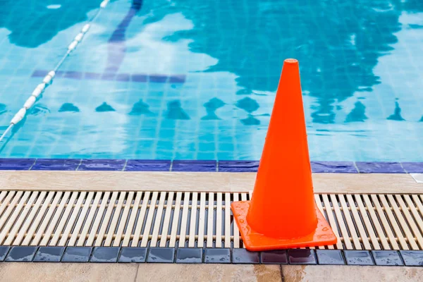 Wet bright orange cone placed by the swimming pool side as safet Stock Picture