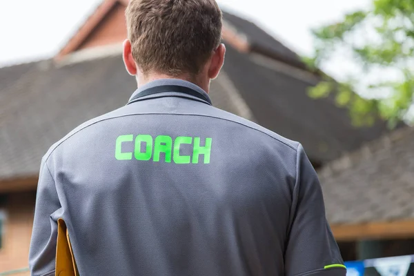 back of a male coach\'s grey shirt with the green word Coach writ