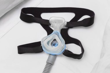CPAP maske, şapka askısı ve beyaz yatakta hava hortumu