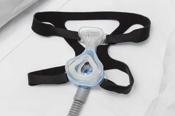 CPAP maske, şapka askısı ve beyaz yatakta hava hortumu