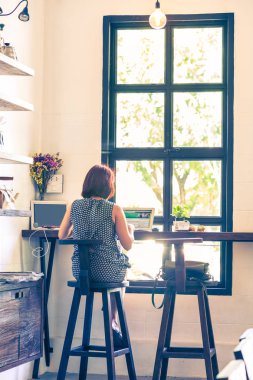 Onu laptop kullanarak büyük bir pencere tarafından oturan bir kadının arka yüzü 