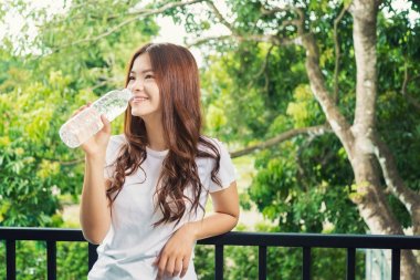 Happy smiling asian woman holding water bottle to drink, standin clipart