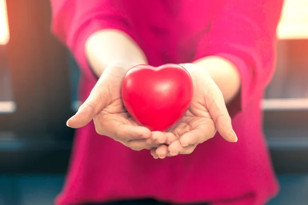 Kobiece ręce trzymając się czerwone serca z tworzywa sztucznego — Zdjęcie stockowe
