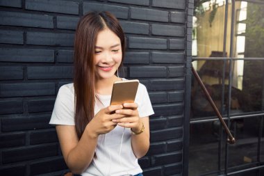 Genç güzel Asyalı kadın akıllı telefonunu dinlemek için wat kullanarak