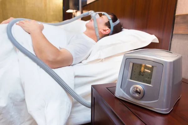 CPAP machine sitting on a bedside table with blurred Middle age — Stock Photo, Image