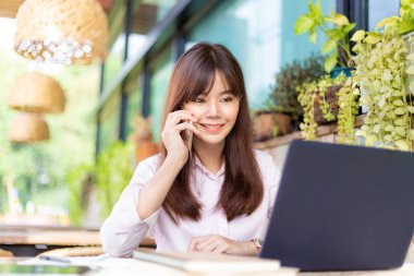 Ofisinin avlusunda bilgisayarında çalışırken telefonunu kullanan pembe tişörtlü, mutlu, genç ve çekici bir iş kadını.