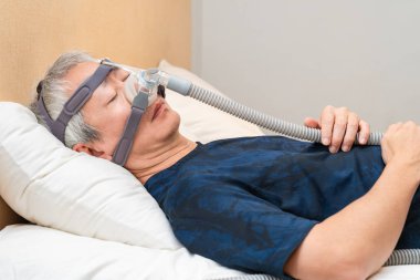 Orta yaşlı Asyalı adam uyurken Cpap başlık takıyor.